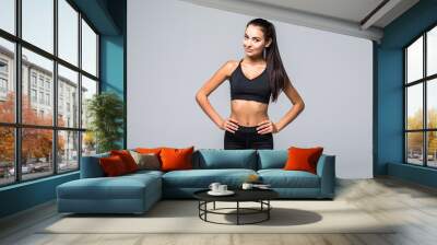 Portrait of sexy young woman with her hands on hips looking at camera. Fitness female with muscular body ready wearing hand gloves for workout on grey background Wall mural